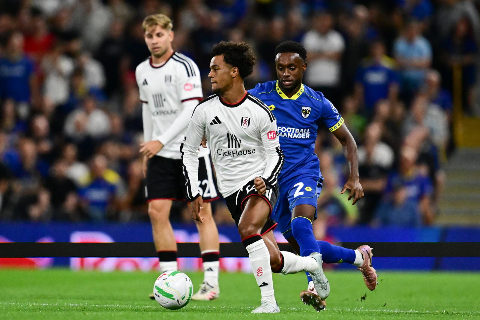Fulham midfielder Oscar Bobb (14) sprints forward with the ball under pressure from AFC Wimbledon defender Stephen Sessegnon (2) during the EFL Cup match between Fulham and AFC Wimbledon at Craven Cottage, London, UK on 27 August 2026.